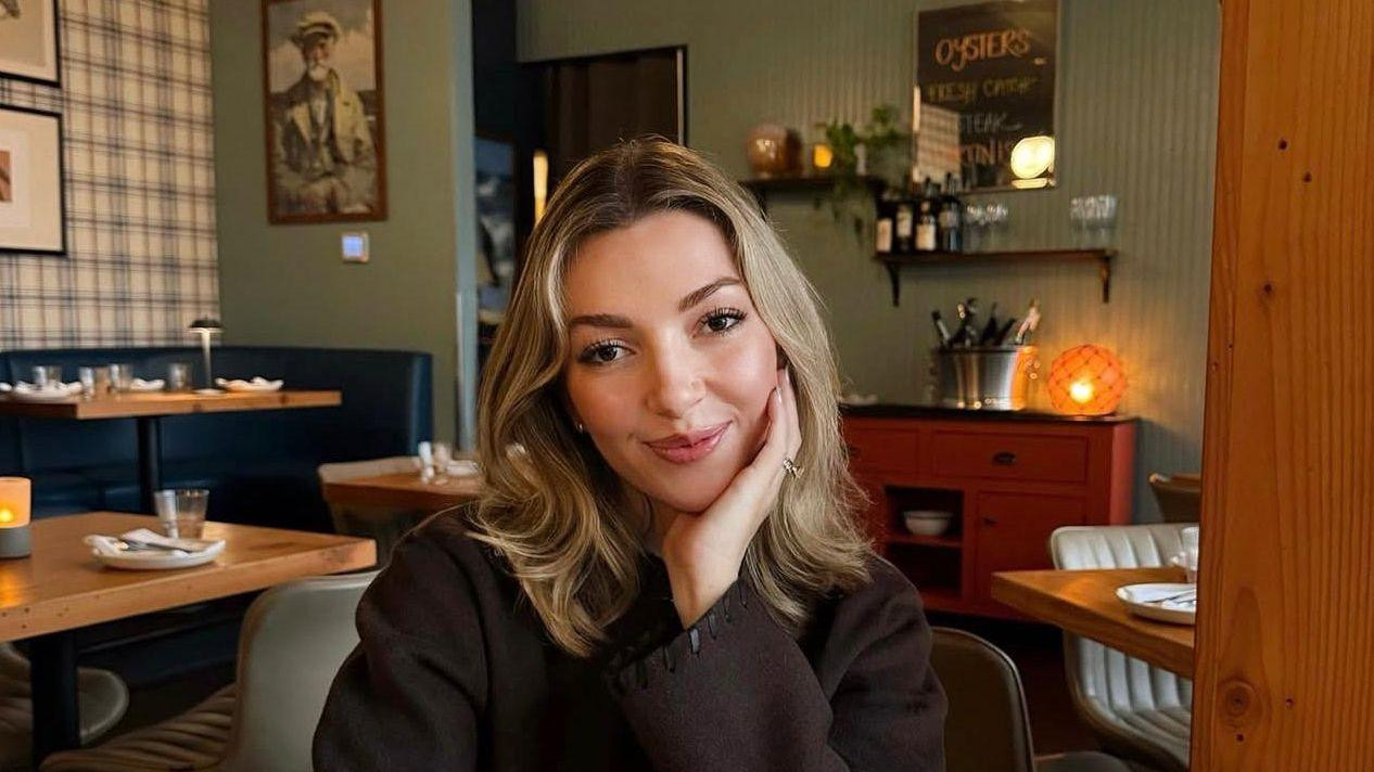 Ginger Smith sits at a restaurant table, with a cocktail and a plate of oysters 
