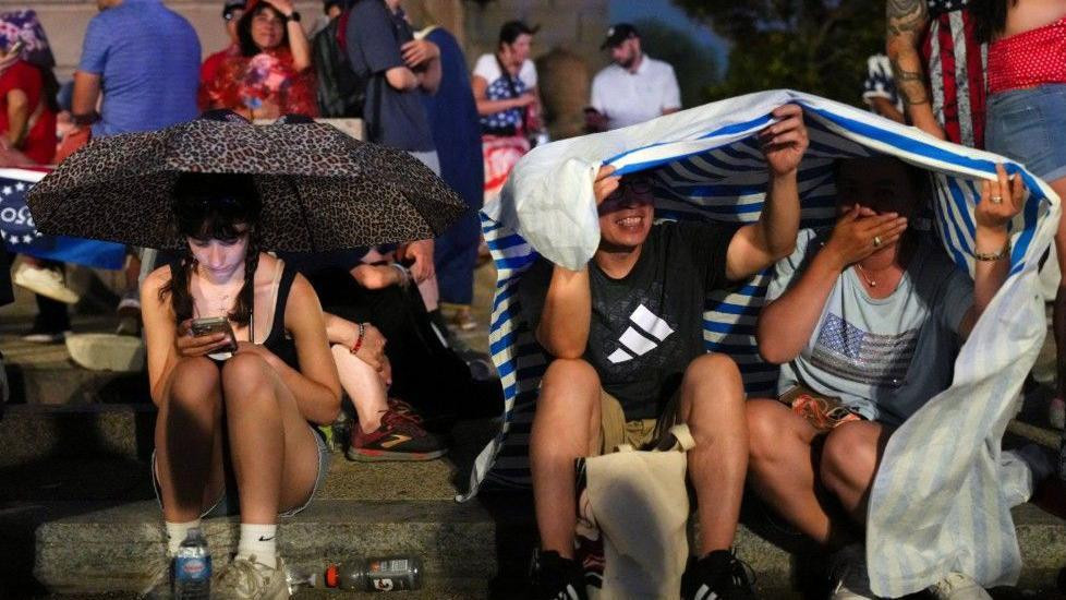 Ljudi se kriju od kiše usled oluje pre početka govora Donalda Trampa, u Vašingtonu 4. jula 2026.