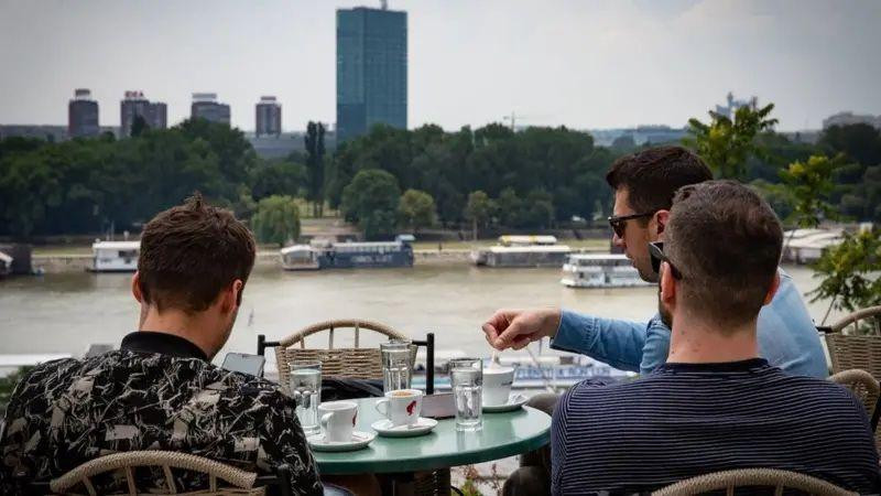 trojica mladića sede i piju kafu u restoranu u beogradu