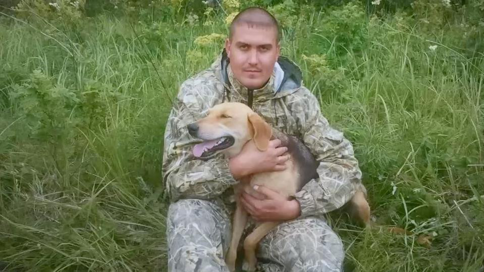 Muškarac sa psom u rukama na travi u vojničkoj trenerci