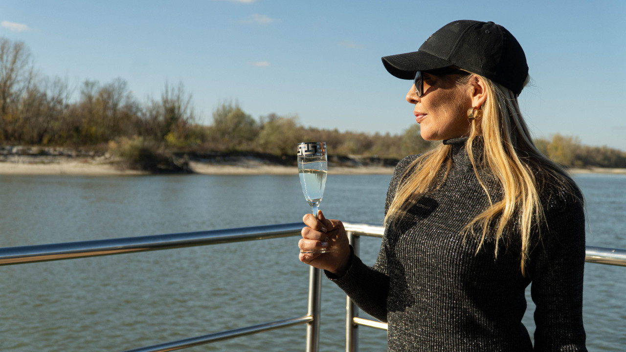 Žena sa čašom u desnoj ruci i naočarima za sunce gleda u reku 