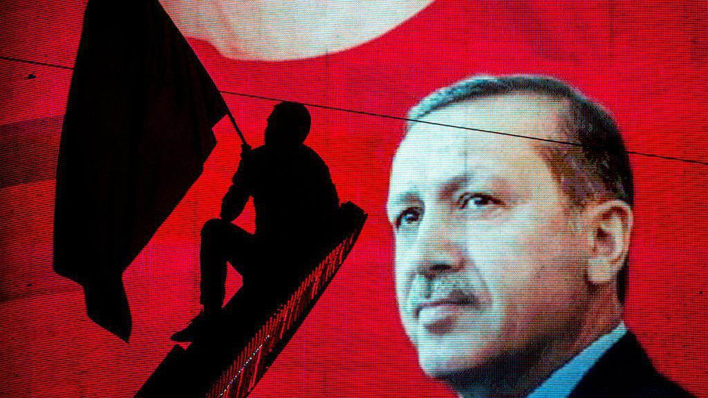 erdogan u krupnom planu, na crvenoj pozadini je silueta muškarca sa zastavom, turska, erdogan, piokušaj puča u Turskoj