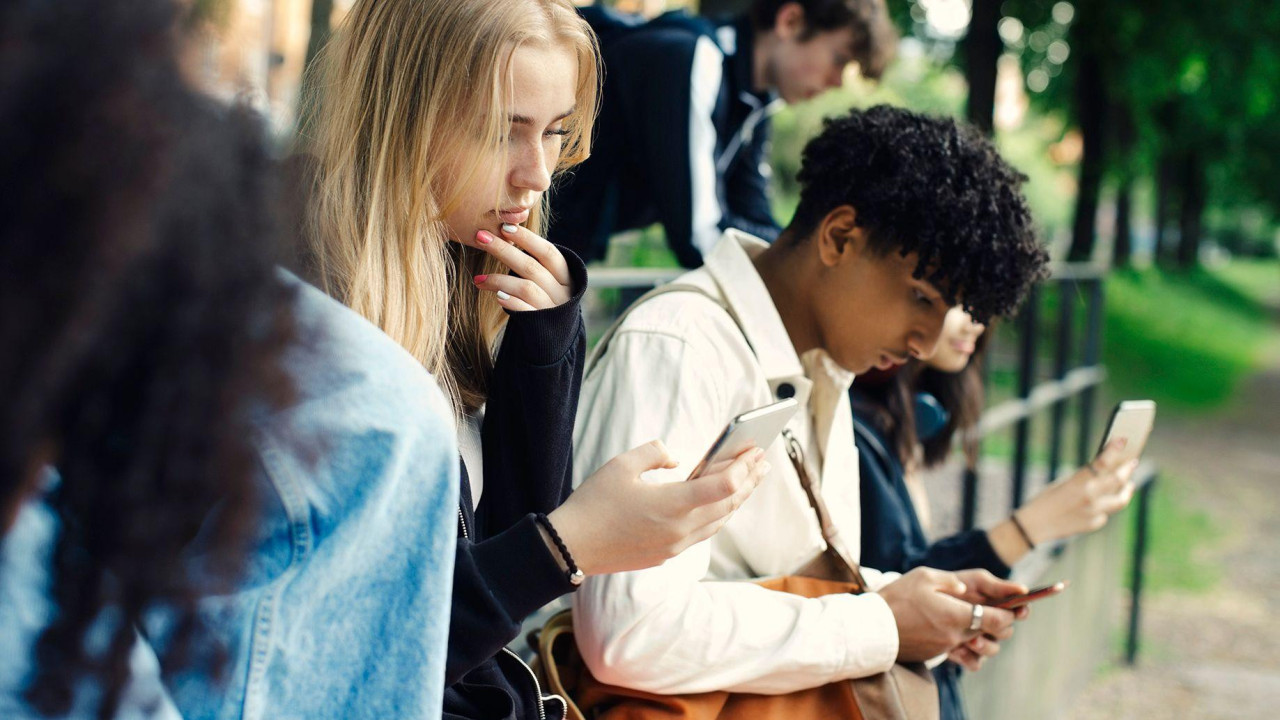 Stock photo shows teens outside looking at phones