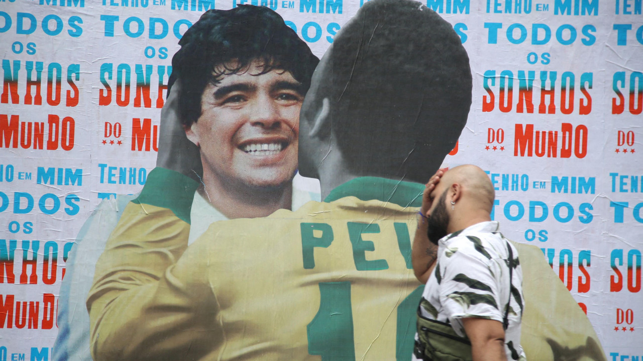 maradona i pele, muškarac prolazi pored kolaža napravljenog od fotografija maradone i pelea