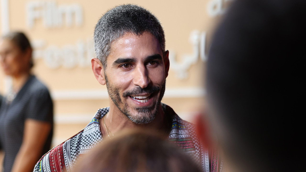 Ahmed Šihab-Eldin prisustvuje otvaranju filmskog festivala u Dohi 2025. On se osmehuje dok razgovara sa ljudima čije su glave u mekom fokusu u prvom planu slike. Žena stoji u daljini.