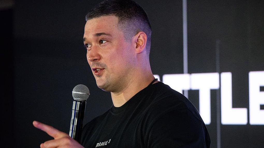 Fedorov drži mikrofon i govori, nosi crnu majicu 
