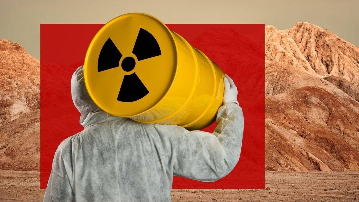 na slici je radnik u zaštitnom odelu koji nosi žuto bure sa međunarodnim simbolom za nuklearnu energiju, u pozadini je gola planina
