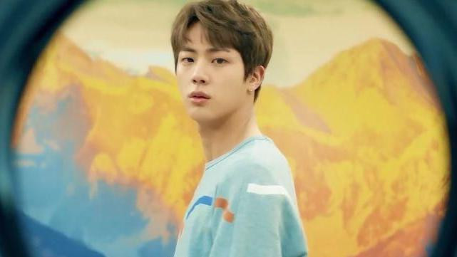 A star from K-pop band BTS looks down the barrel of the camera, with yellow tinged mountains behind him