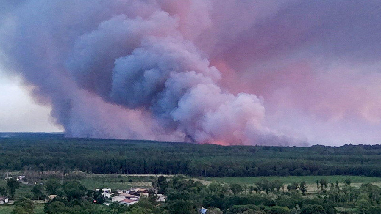 A drone view showing the Sainte-Helene commune in France with smoke rising in the background during a wildfire in a forest area in Saumos