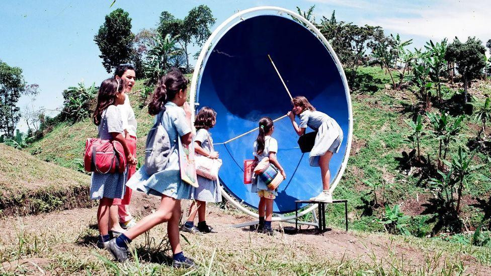 Deca se igraju napolju, jedna devojčica stoji ispred plavog satelita