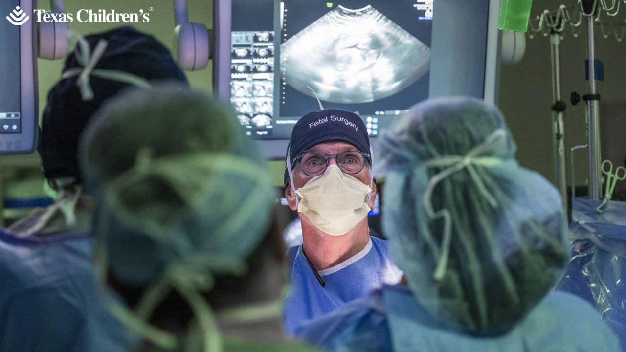 Lekar sa maskom na licu i zaštitnim naočarima gleda u tablu, oko njega je nekoliko medicinskih sestara 