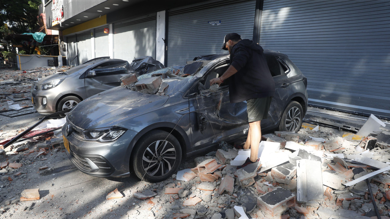 Čovek stoji pored uništenog automobila posle zemljotresa