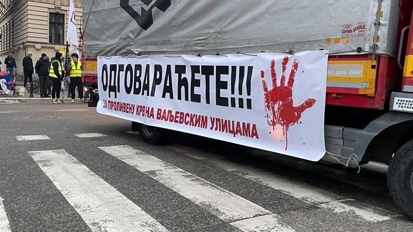 Na belom transparentu prikačenom za kamion ispisano je 'Odgovaraćete za prolivenu krv na valjevskim ulicama sa crvenom šakom'