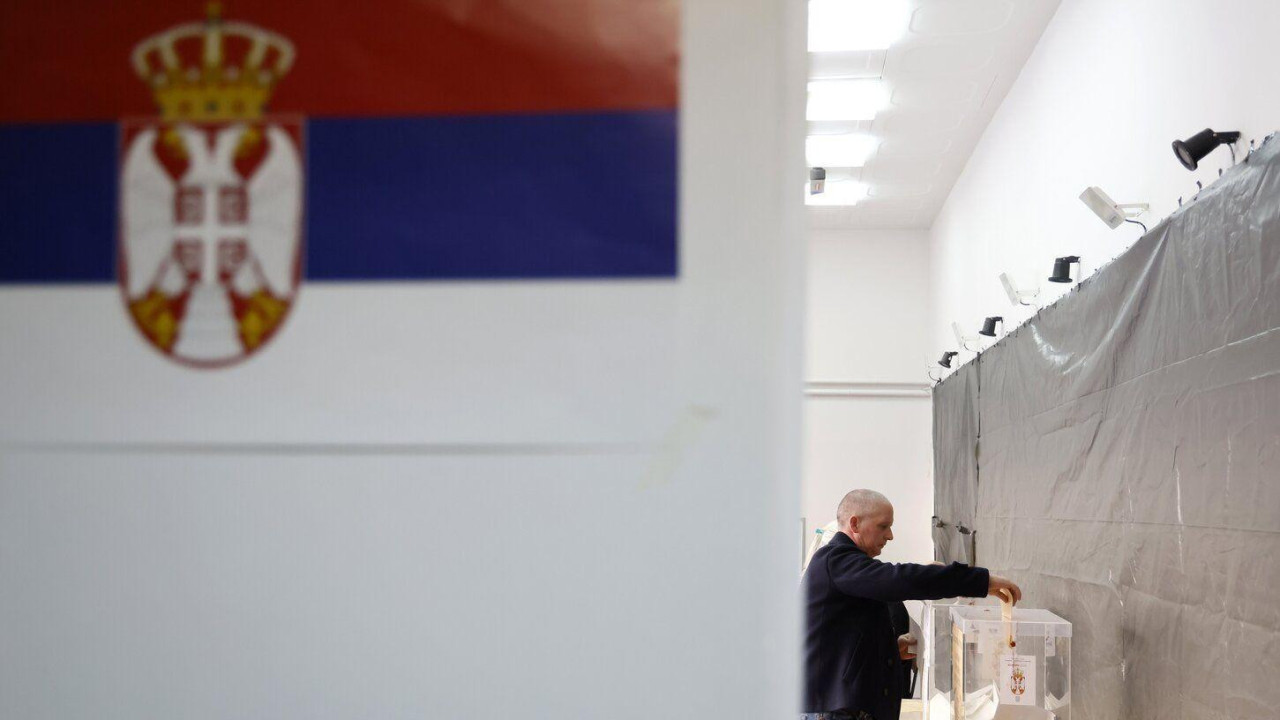 Čovek ubacuje glasački listić u kutiju u krupnom planu zastava Srbije