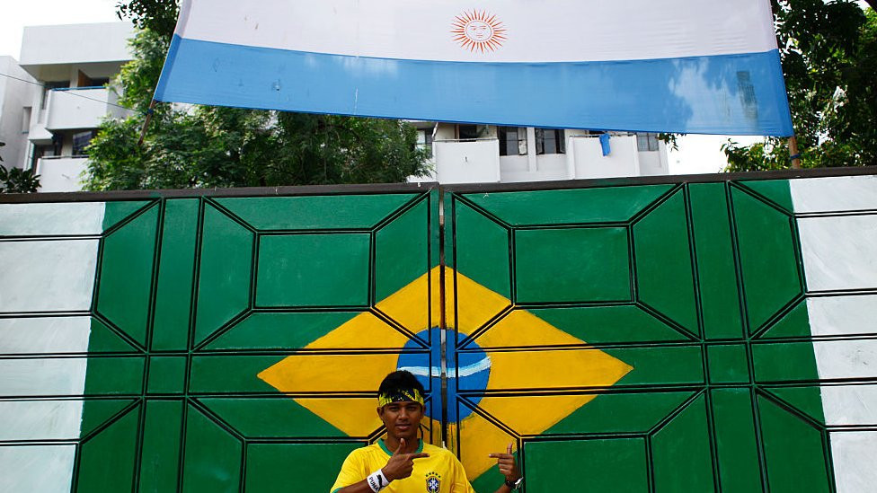 Persona fotografiándose con las banderas de Brasil y Argentina en Bangladesh.