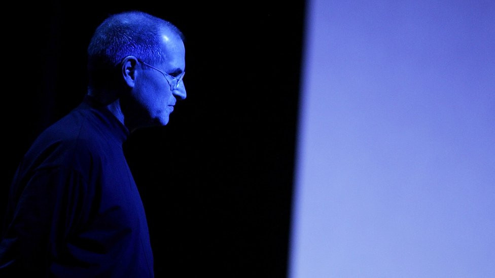 Steve Jobs lit up by blue lighting at a press event.