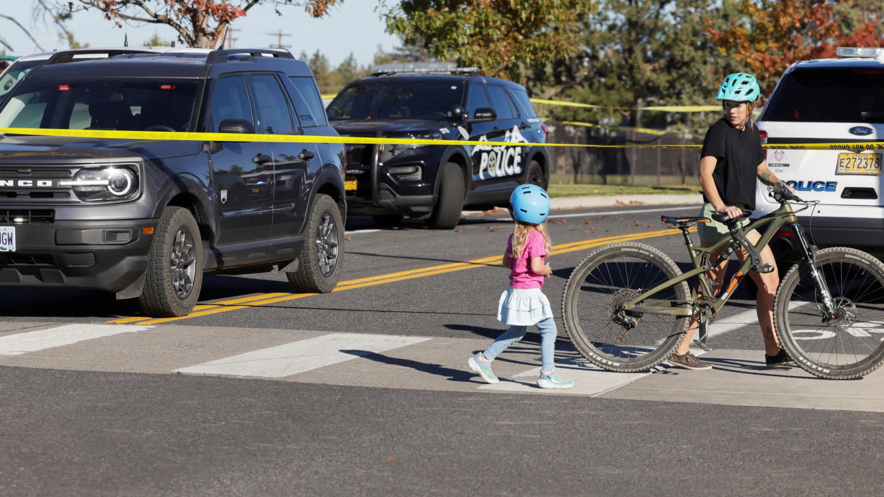 A girl and woman cross the road with police cars and tape in the background