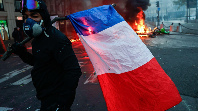 Demonstrant drži zastavu, vatra iza njega